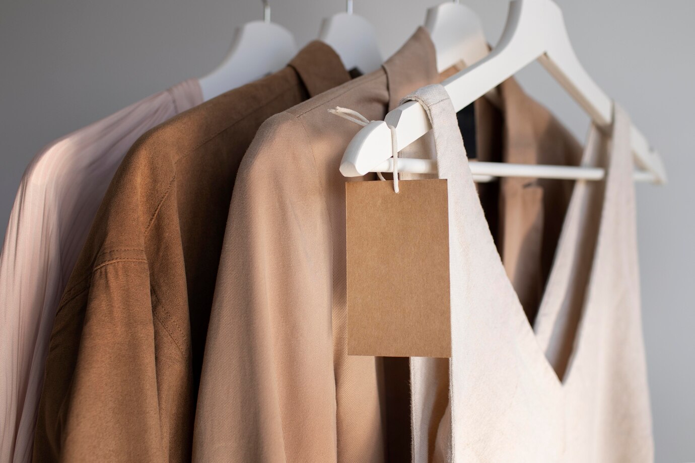 A close-up of hanging clothing in neutral shades, featuring a blank price tag on a white dress for potential pricing or branding.