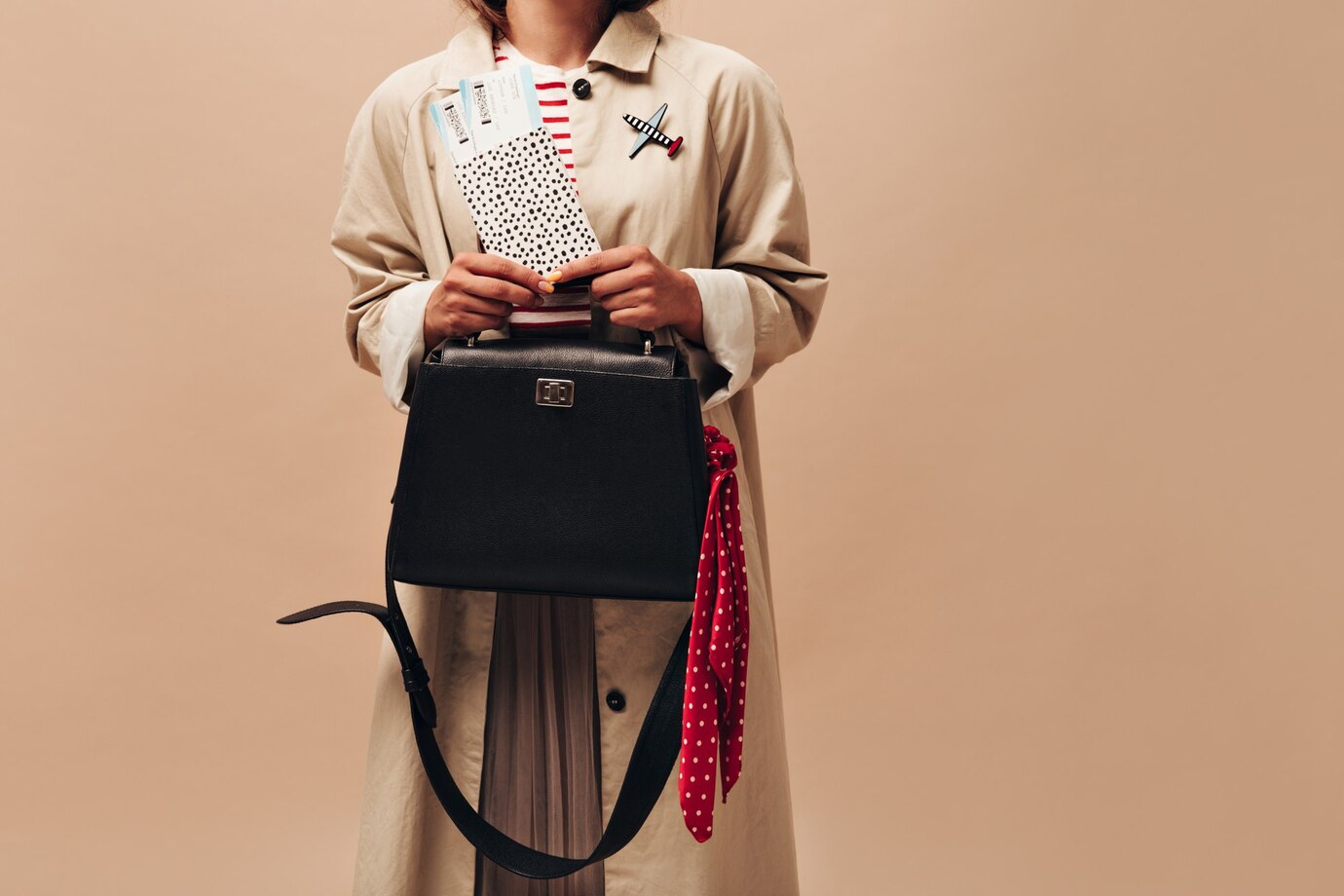 A woman in a beige trench coat holds a black handbag