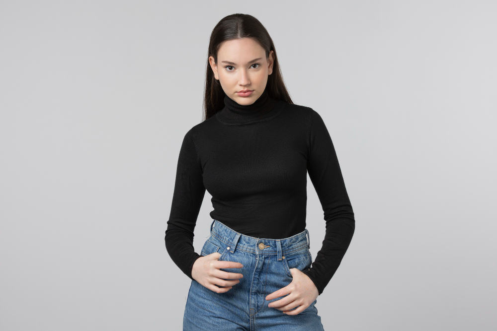 A young woman poses confidently in a fitted black turtleneck and high-waisted denim jeans.