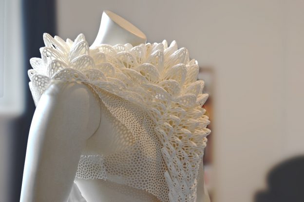 A close-up of a mannequin showcasing an intricate, white lace design garment with a collar.