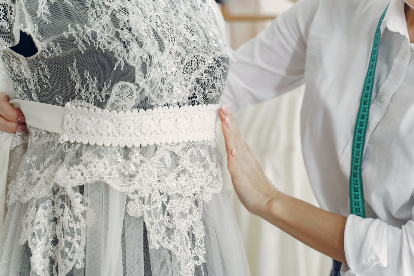  dressmaker adjusts a delicate lace wedding dress