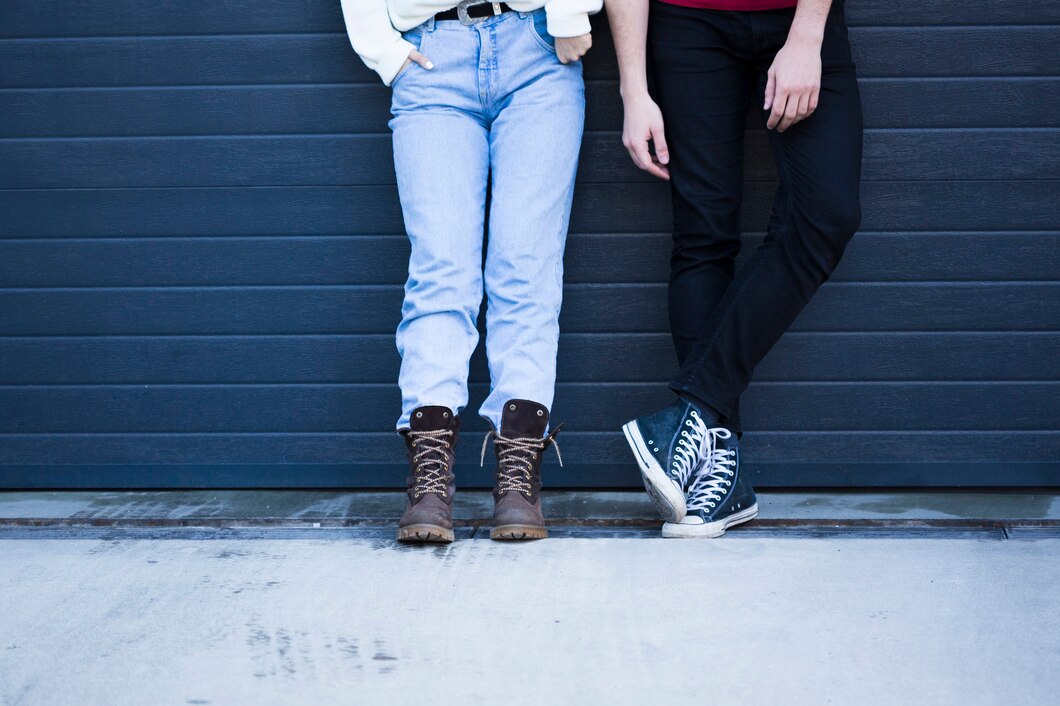 A close-up of two pairs shoes and blue jeans, the other in black pants and high-top sneakers.