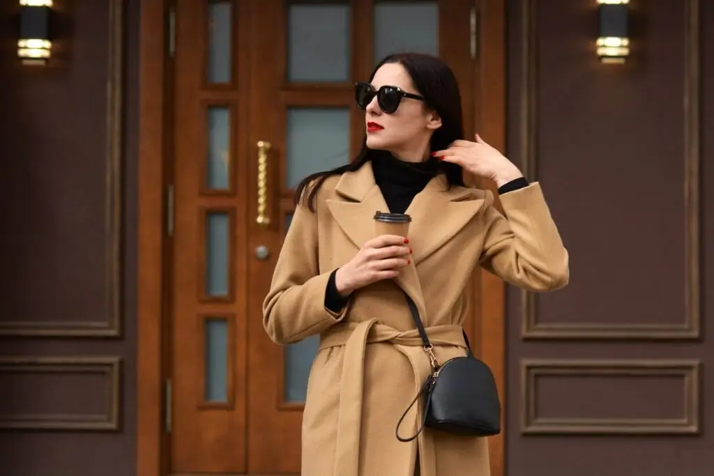 woman in a stylish beige coat holds a coffee cup,