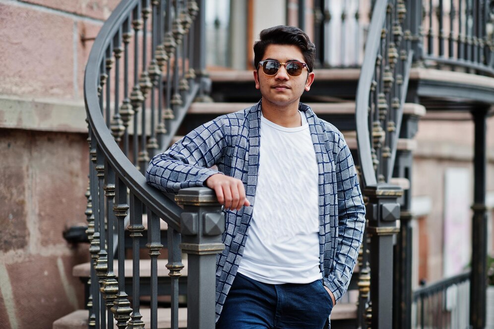 Young man in sunglasses and casual jacket standing on urban stairs, looking confident.