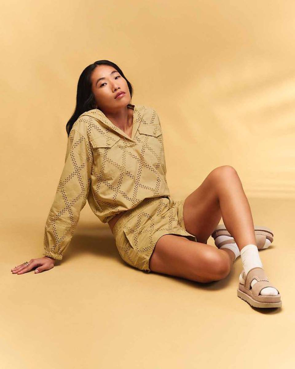 Woman in a patterned yellow outfit sitting elegantly against a matching yellow background.